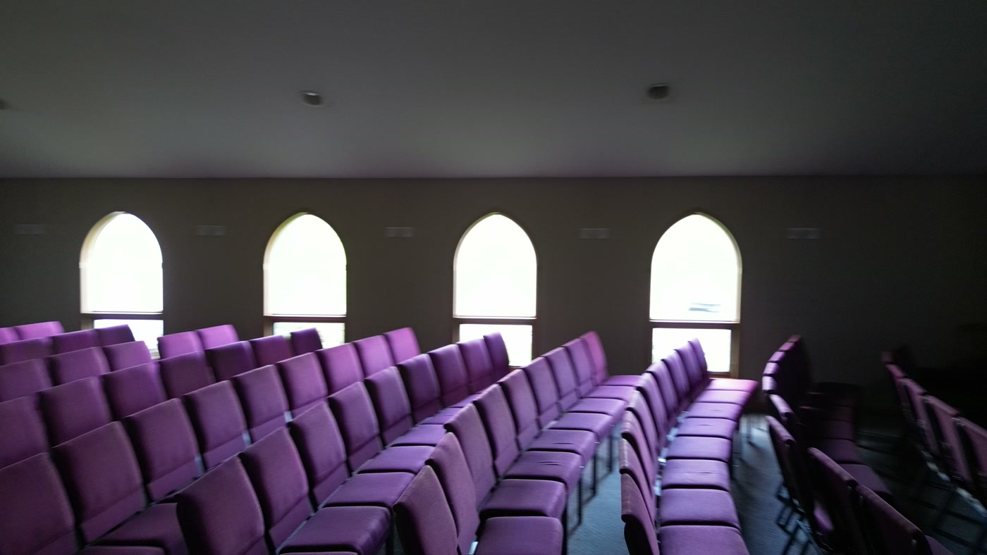 Rows of purple upholstered chairs on the sanctuary floor at St. Peter's, the chancel and its lit window at the far end