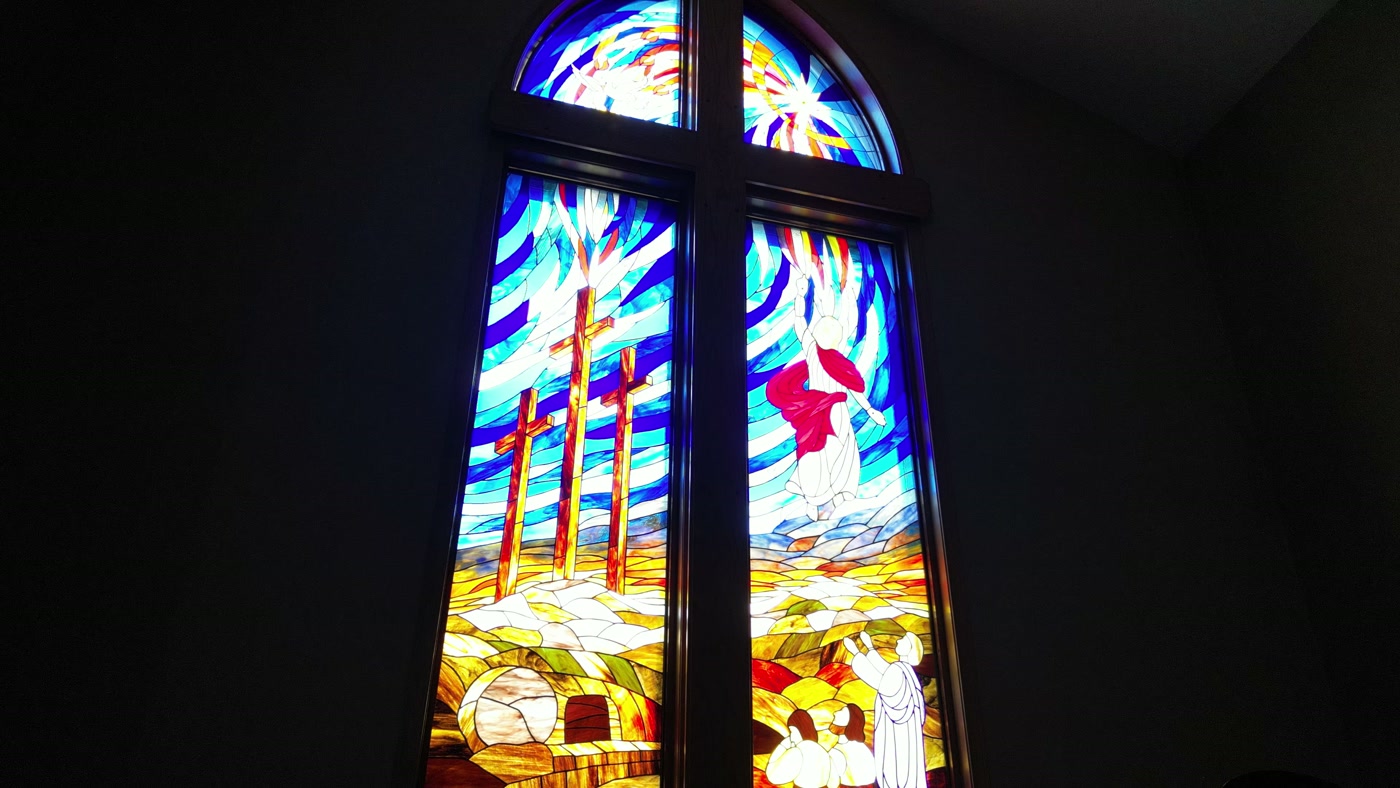 The lower lights of the window at St. Peter's: three crosses on a golden hill, a tomb cut into the rock with its stone rolled aside, and figures below with their hands raised