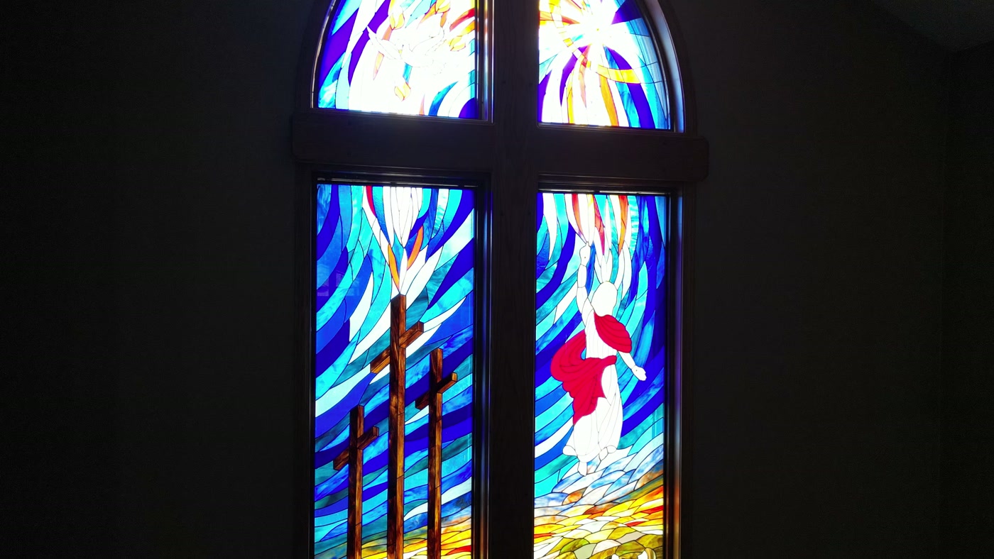 The stained-glass window above the chancel at St. Peter's Lutheran Church, Cochrane: three crosses on a hill, a figure in white and red rising above them, blue rays across the sky