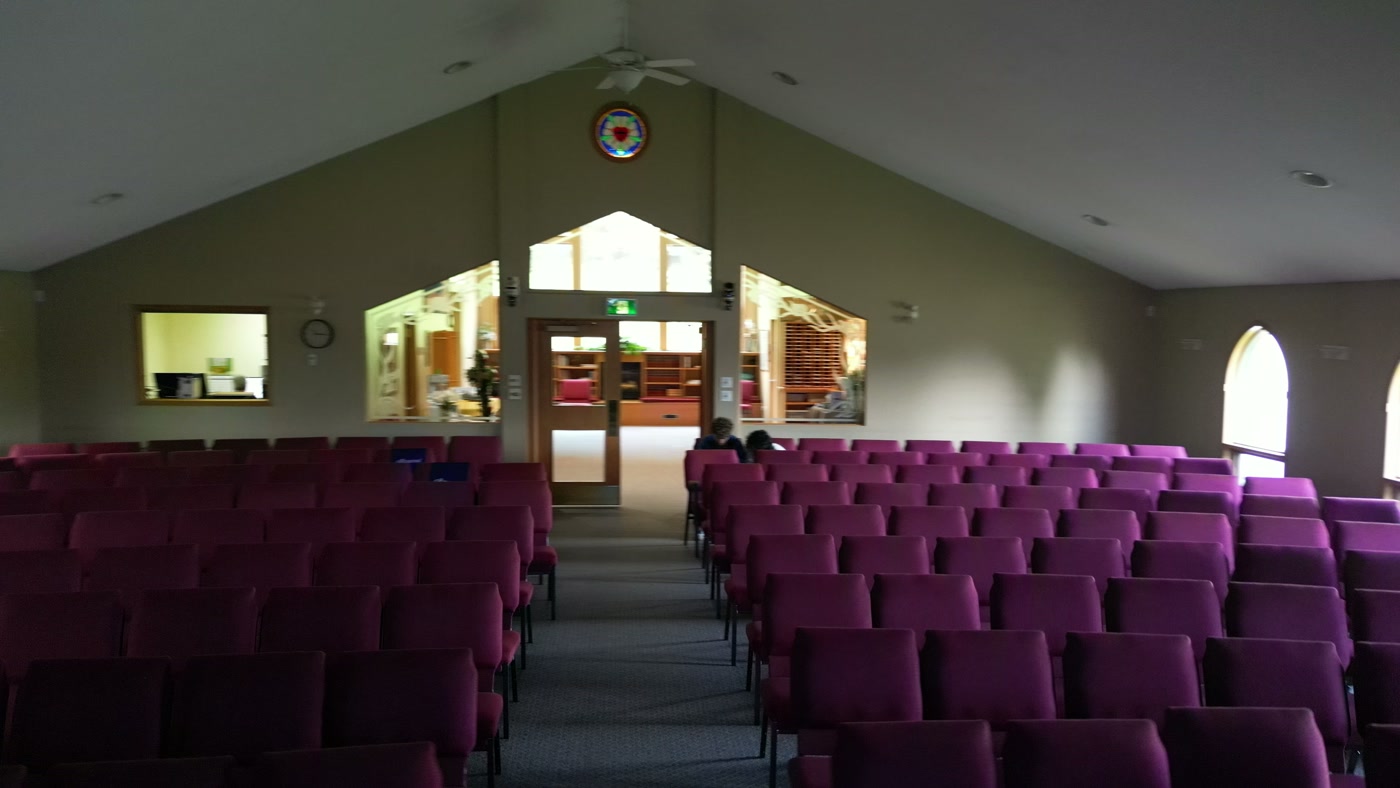 Clear arched windows along the sanctuary wall at St. Peter's in Cochrane, daylight falling across the empty rows of chairs