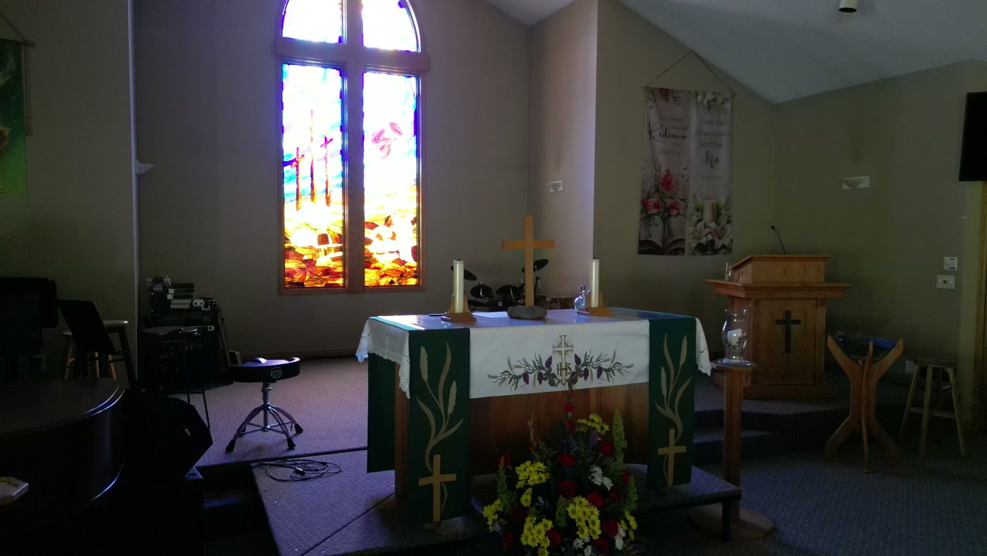 The communion table at St. Peter's under a green frontal worked with wheat and a cross, two lit candles on it and cut flowers on the step below