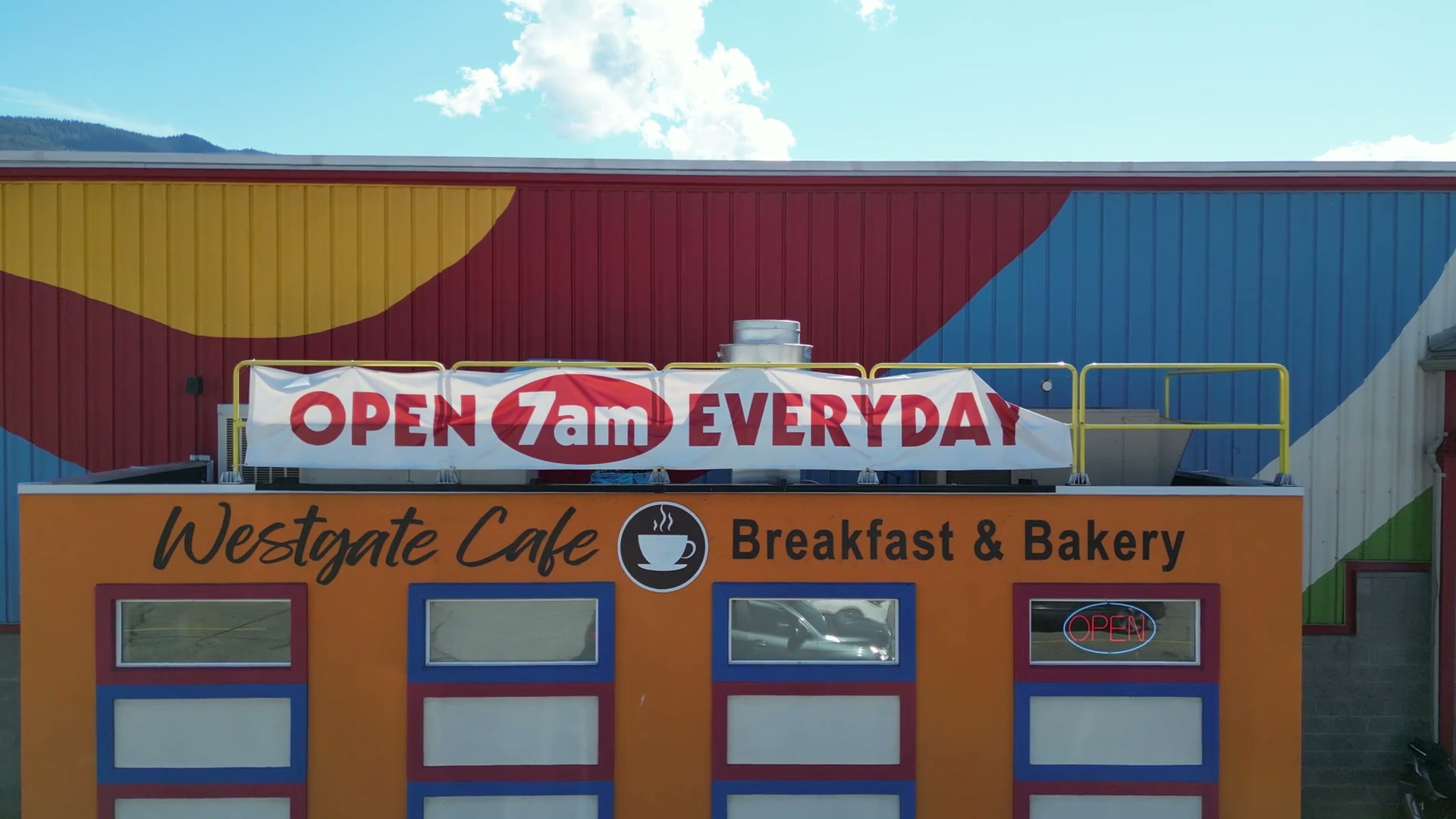 Easing in head-on toward Westgate Cafe in Salmon Arm, at half speed: the name in black script, a painted coffee cup, Breakfast & Bakery, four framed windows, and the banner OPEN 7am EVERYDAY