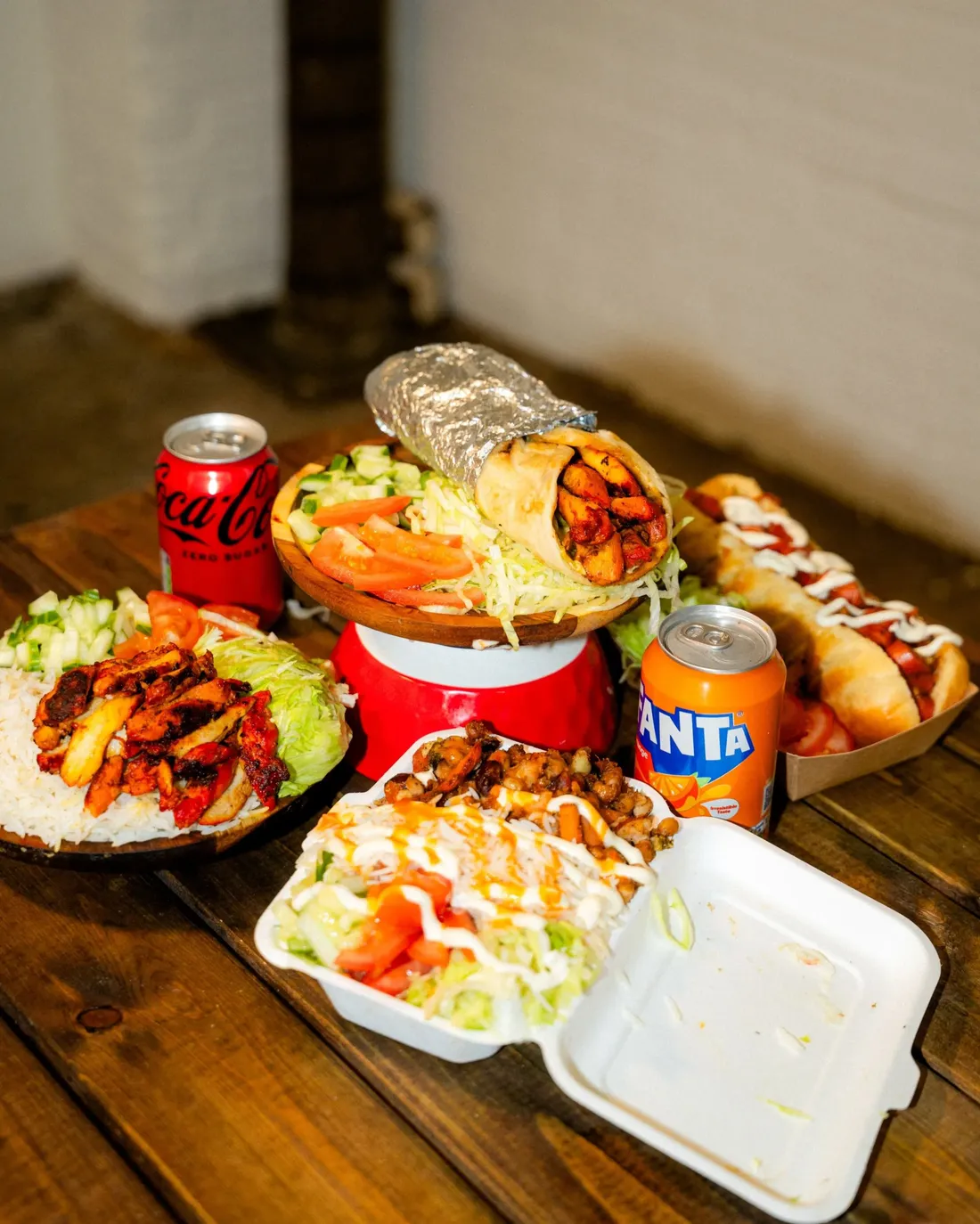 Wraps, rice boxes and cold cans crowded onto a wooden table
