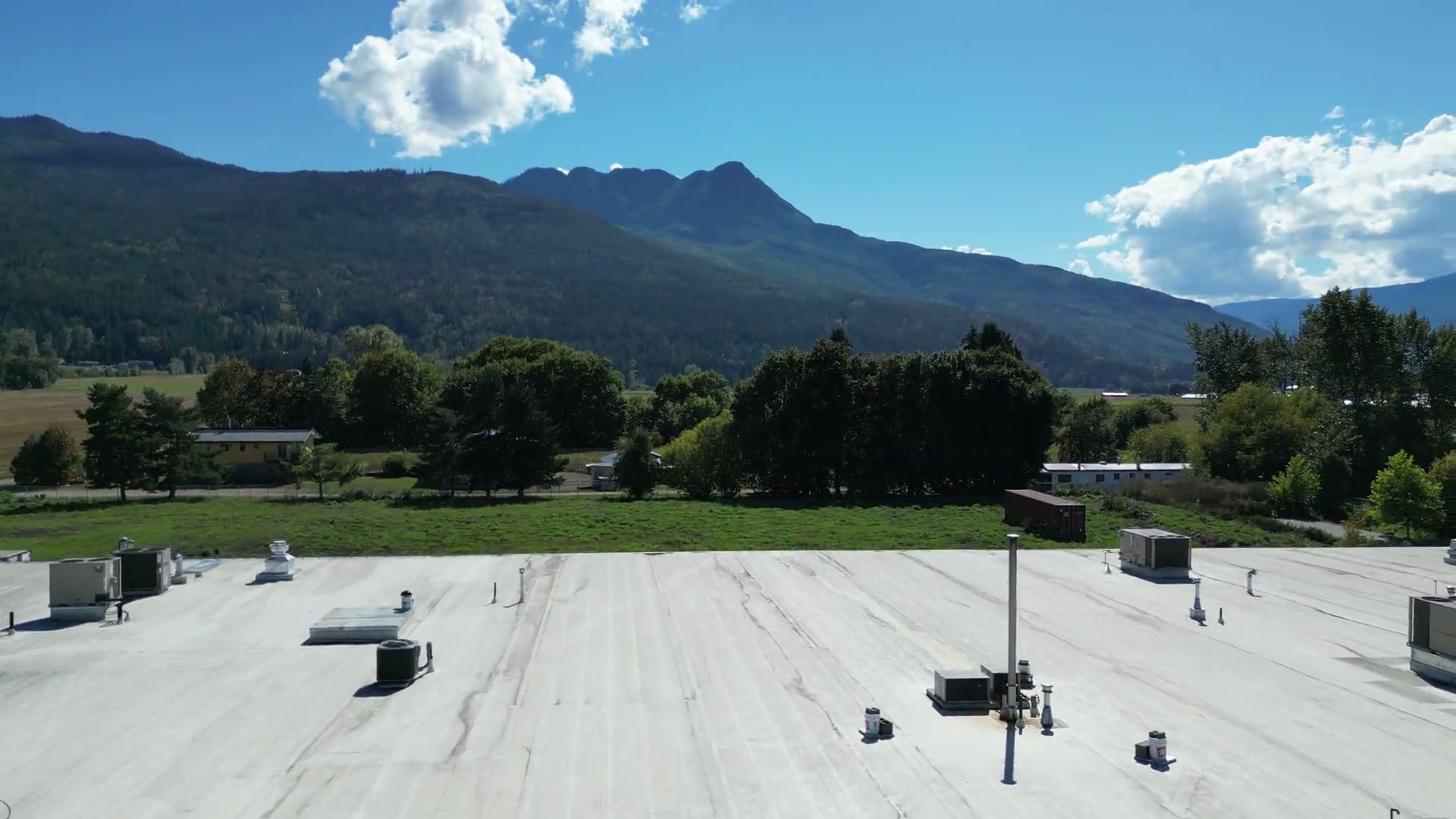 From the lot of Westgate Public Market in Salmon Arm, rising past the café's rooftop banner and the painted metal wall, over the flat roof and out across the fields toward Mount Ida