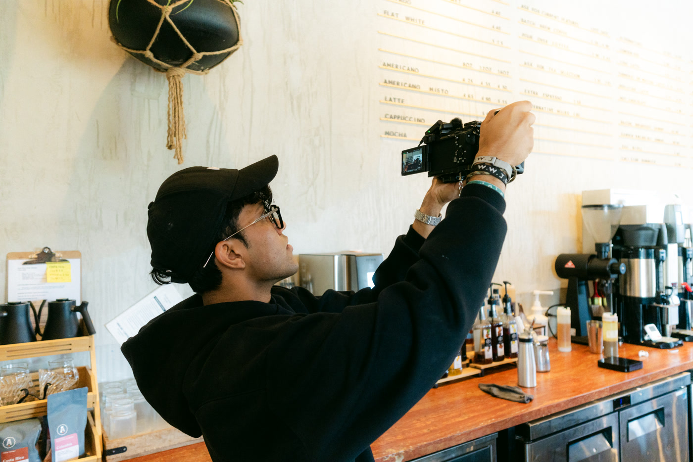 A camera raised to photograph the letterboard menu from below, the brew bar and syrup bottles along the counter