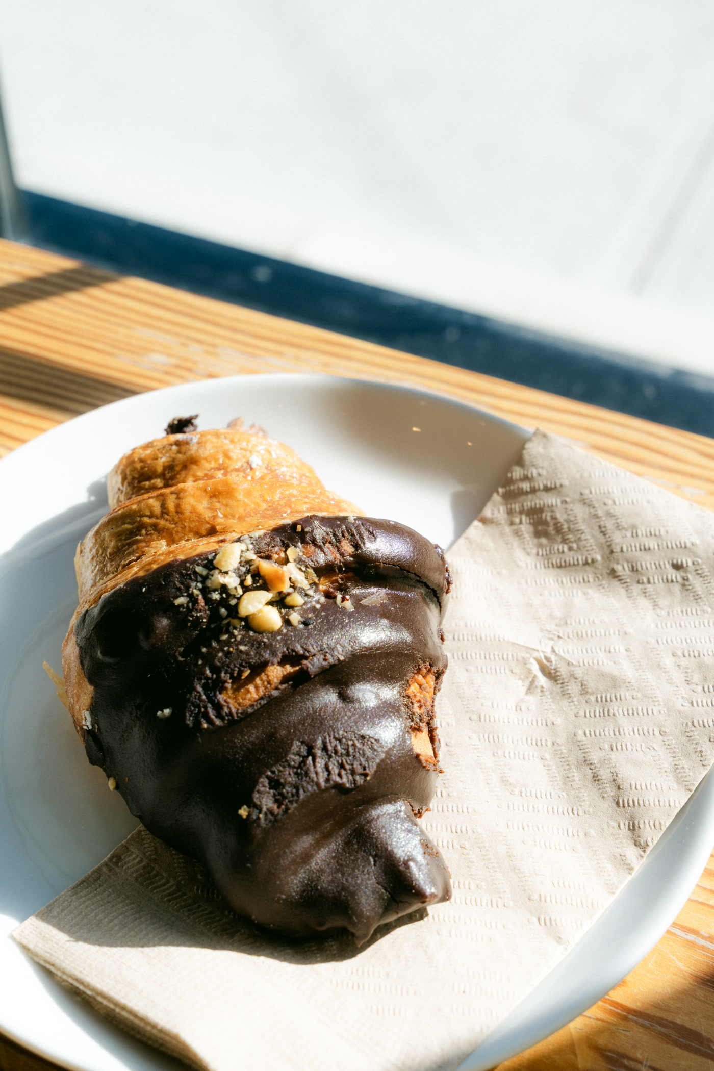 A chocolate-dipped croissant on a white plate, the patio table's grain and shadow beneath it