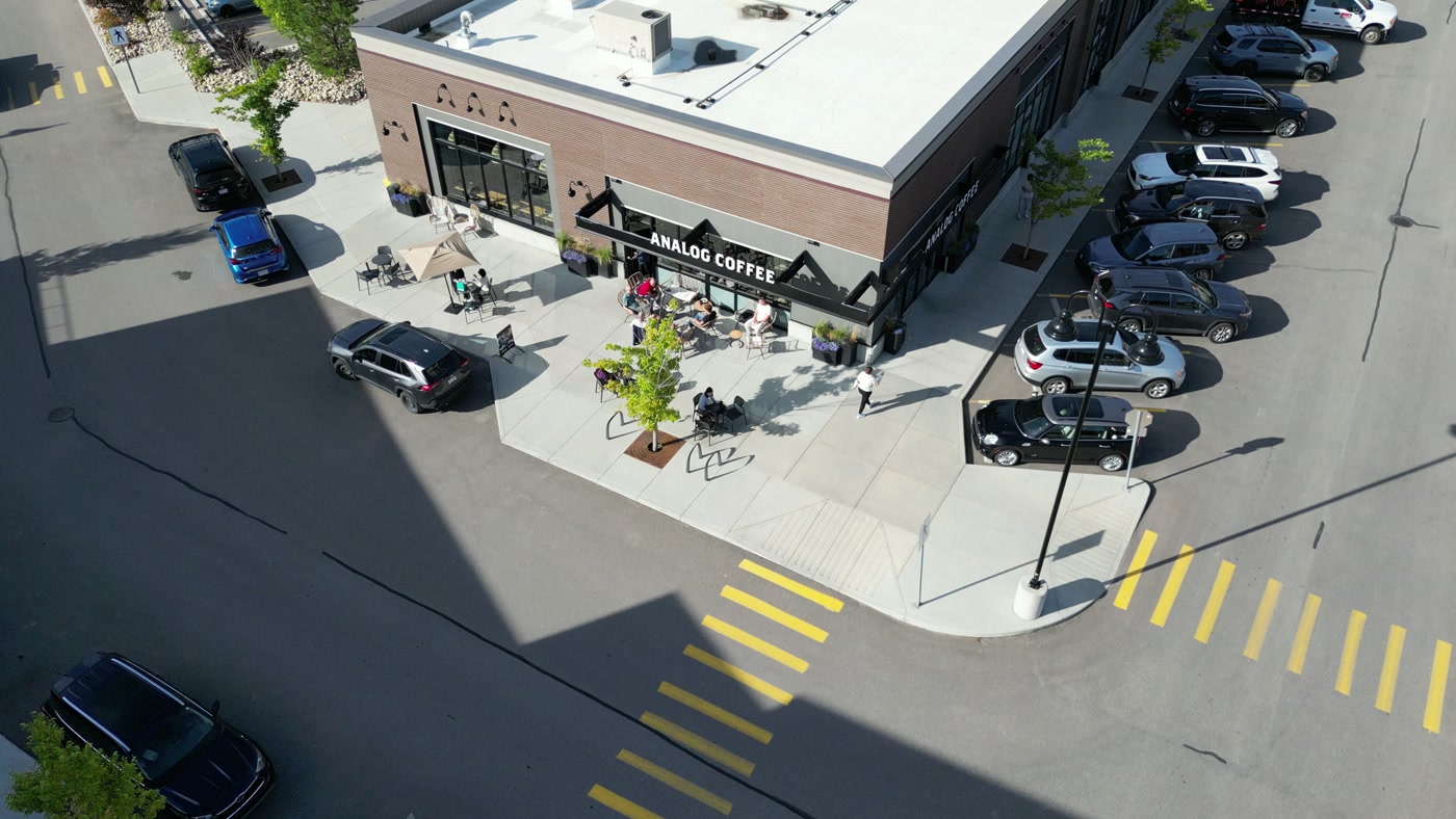 The corner unit from high above: the patio's tables and bike rack, the yellow crosswalk bars, the lot and the trees along the sidewalk