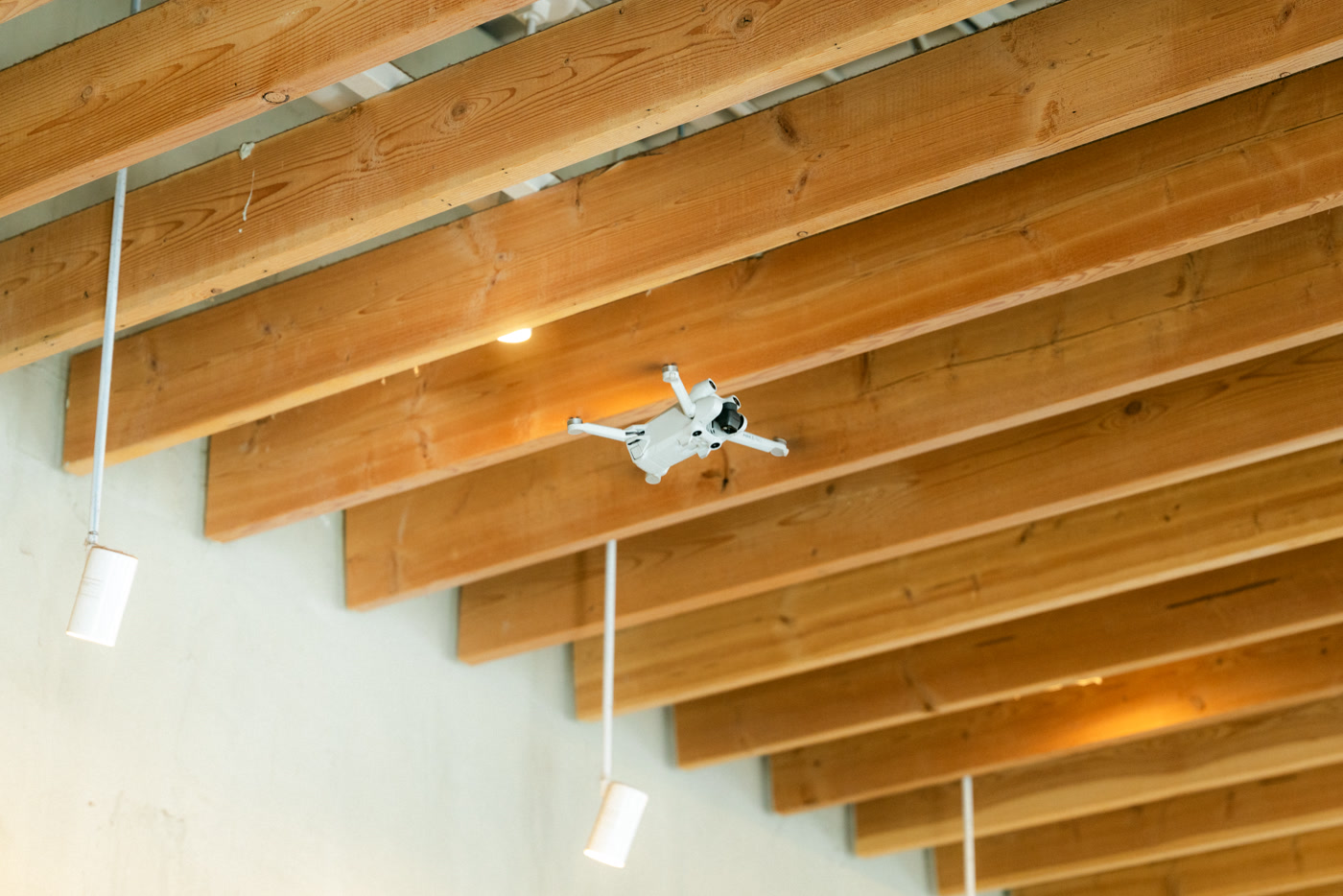 The drone in mid-air inside the cafe, hanging between the timber ceiling joists under the pendant lights
