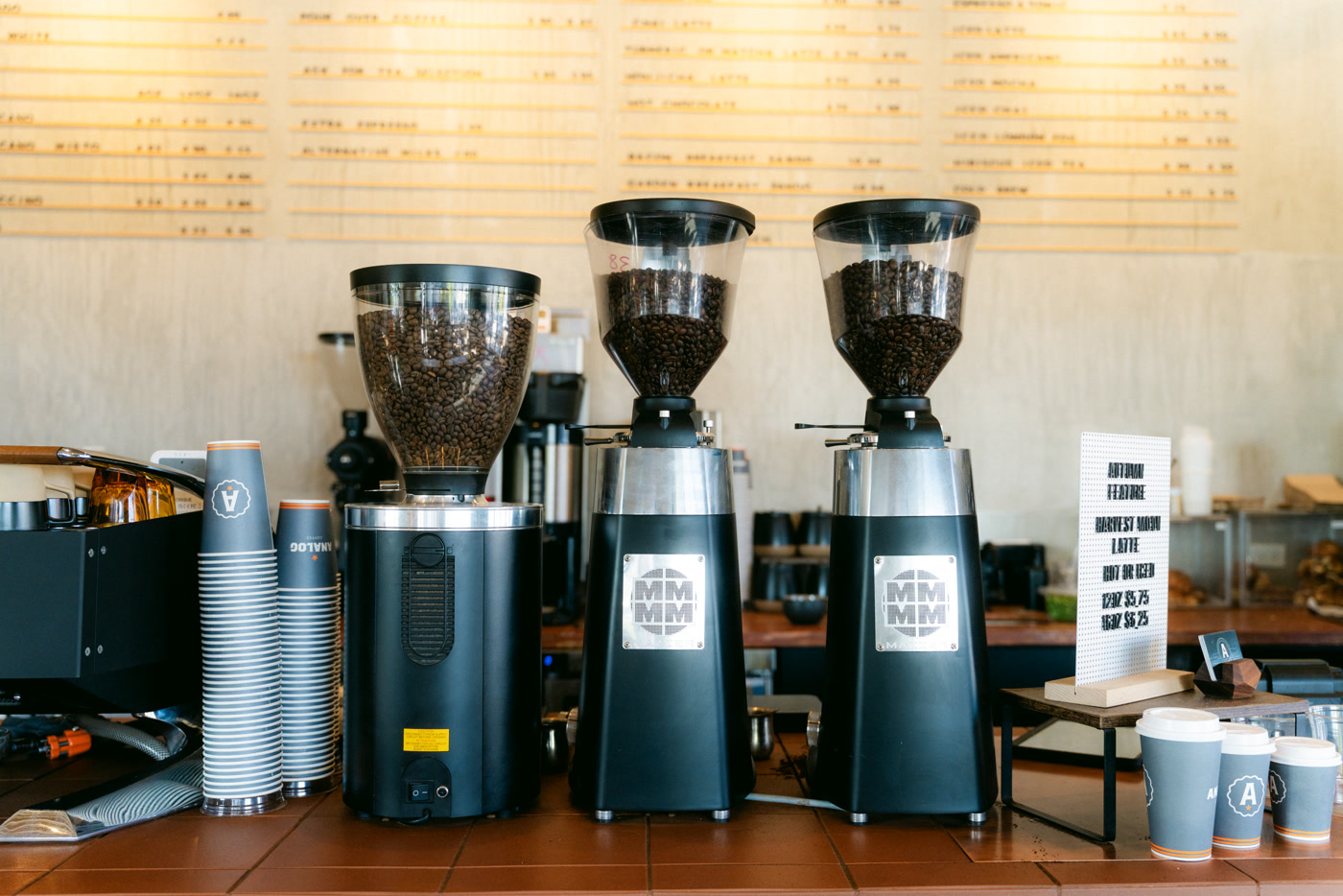 Two grinders with their hoppers full of beans on the copper-tiled counter, stacked cups and the brew bar beside them