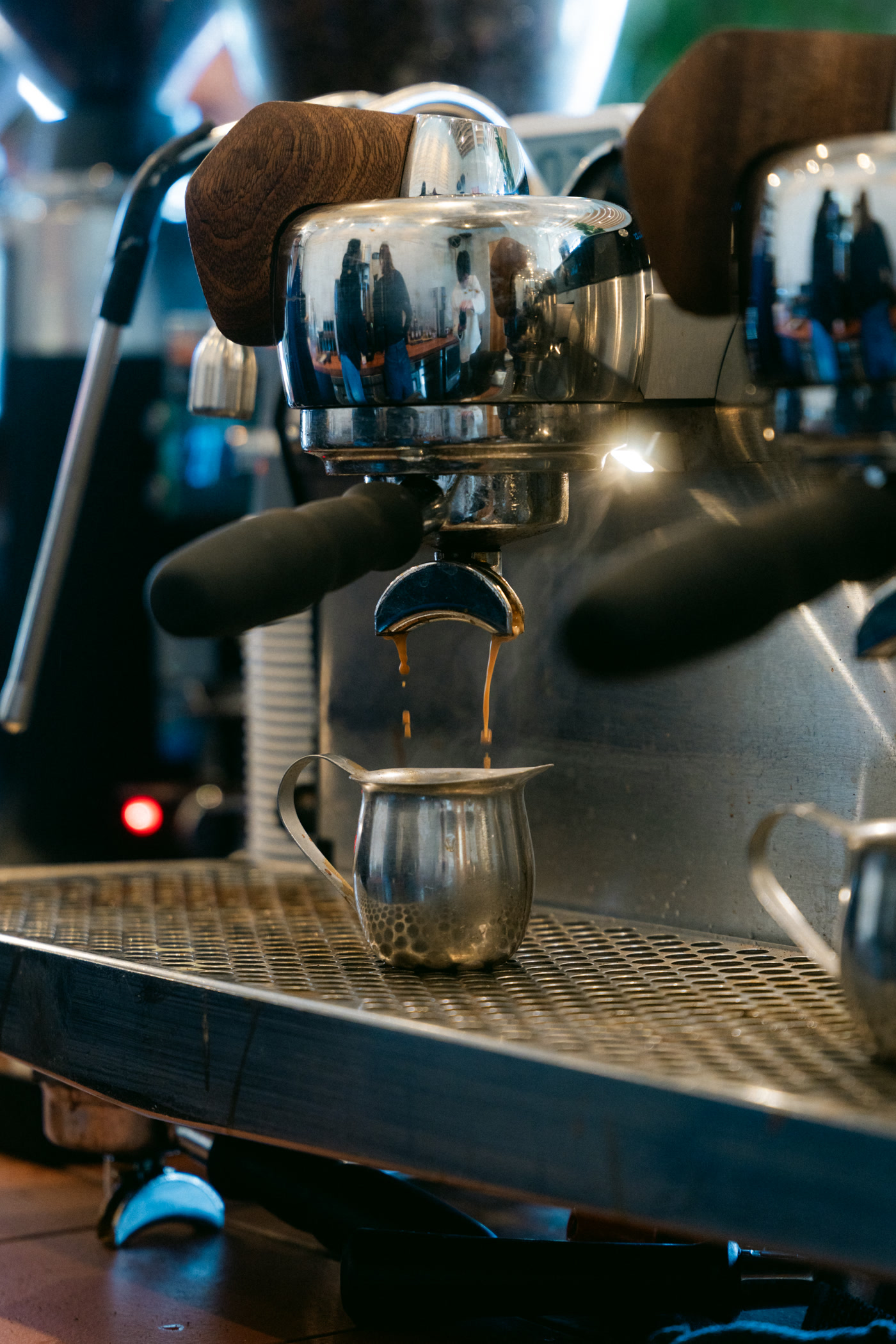 The machine's group head close up, a wooden portafilter handle locked into it and the room reflected in the steel