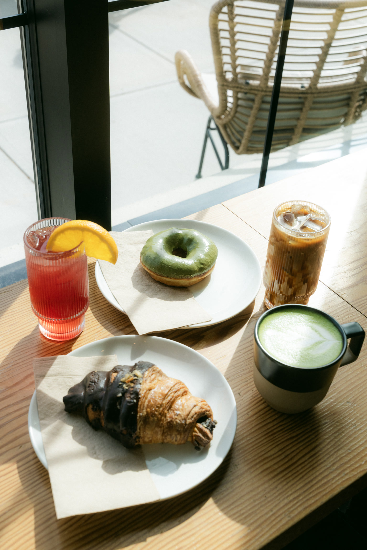 The morning's order closer in: the red drink and its orange slice, the doughnut on its plate, the croissant beyond