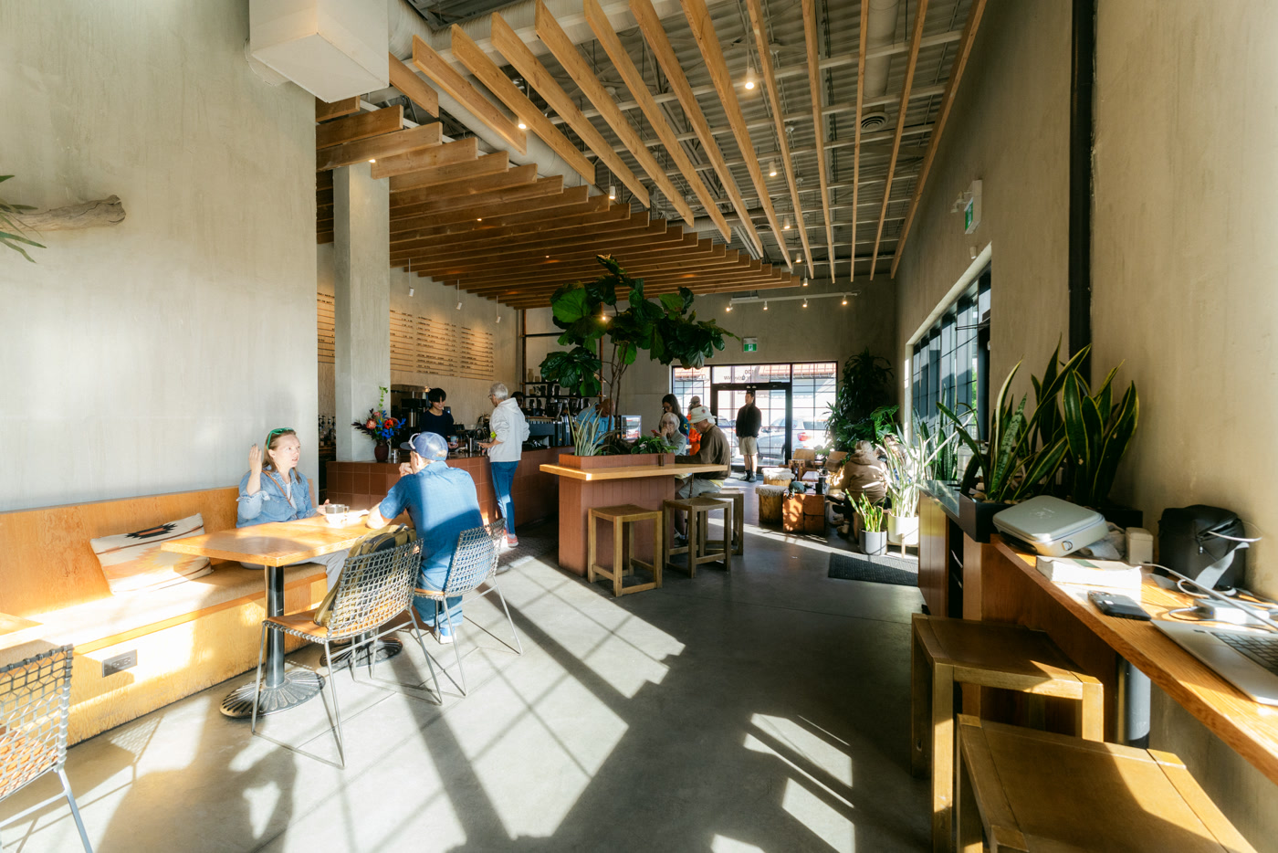 The banquette and tables under the timber-slat ceiling, morning light across the concrete floor