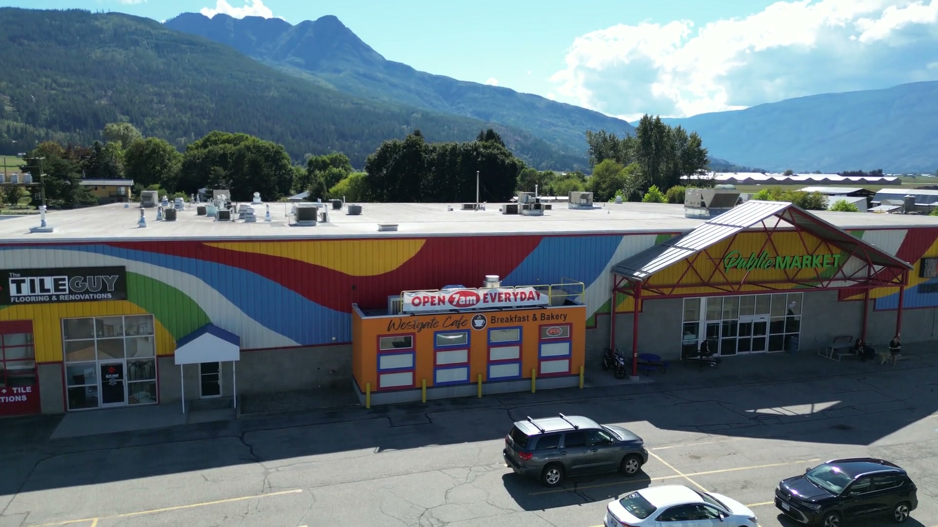 Backing off the flat white roof of Westgate Public Market in Salmon Arm, at half speed, and coming down until the painted bands, the orange café and the red gable fill the frame