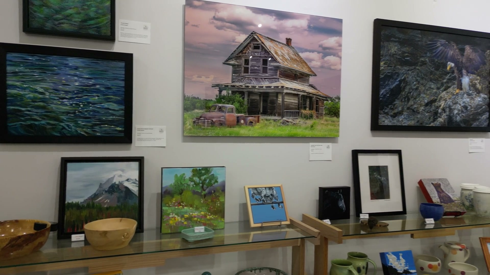 Flying along the hung wall inside Route 22 Art Gallery in Cochrane, past framed paintings and a glass shelf of turned wooden bowls