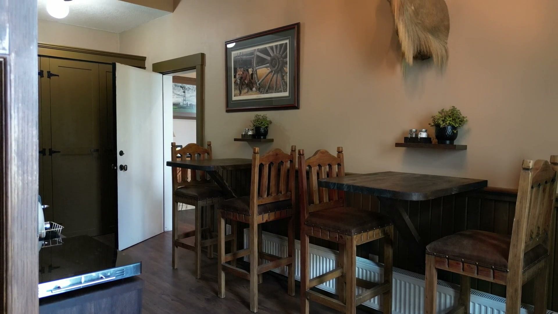 Drifting through the breakfast area of Shire Ridge Lodge near Bragg Creek: wooden tables and tall chairs, a framed print, mounted heads with curled horns and the antler chandelier hanging above