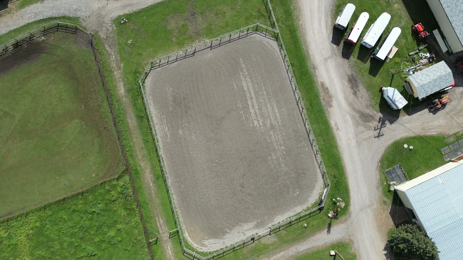 From above, a sand riding ring at Shire Ridge Ranch near Bragg Creek beside grass paddocks, a gravel yard of parked horse trailers and the white roofs of the barn buildings