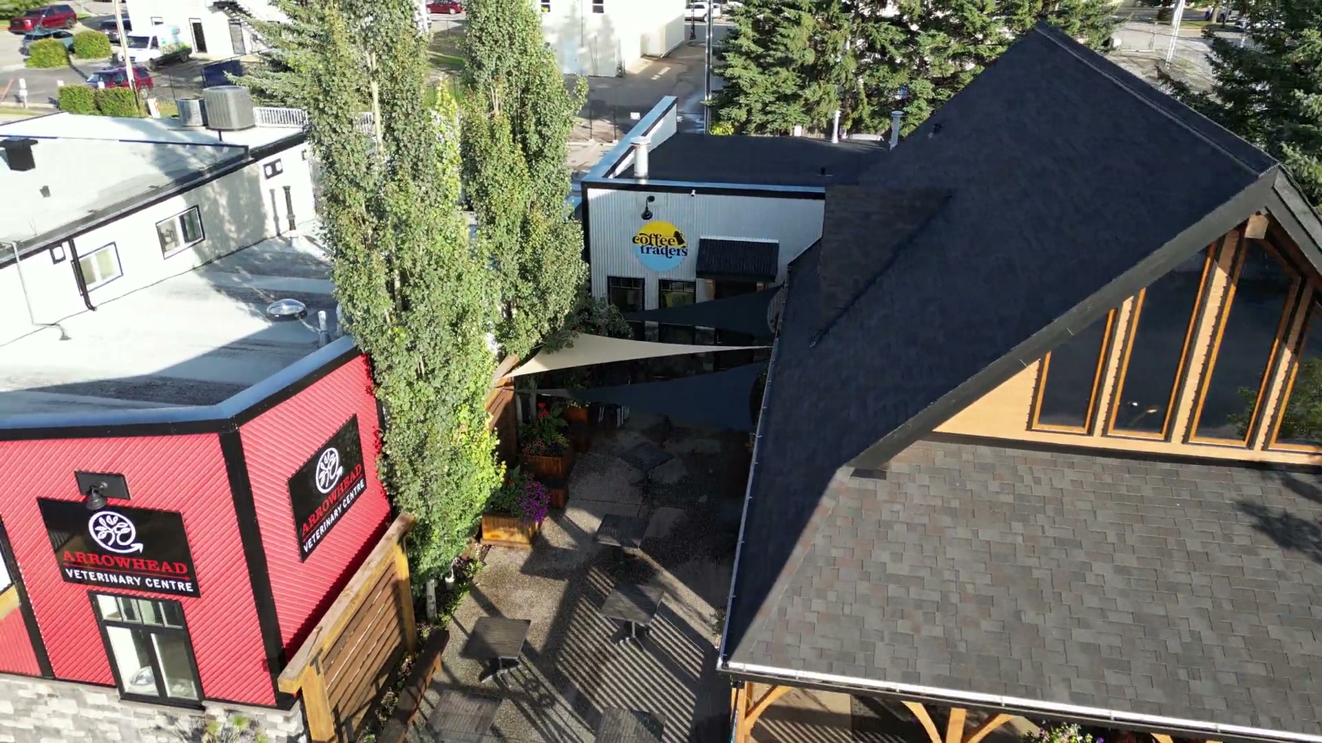 Starting on the round coffee traders sign in the courtyard of Cochrane Coffee Traders and pulling back over the shingled roof and poplars until the porch, its lamp post and the sidewalk appear