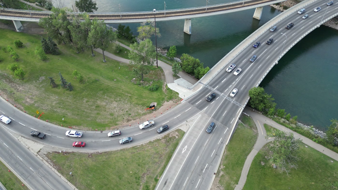 The Reconciliation Bridge's 1972 span and the CTrain bridge beside it from directly above, the Bow River green beneath both, cars mid-crossing