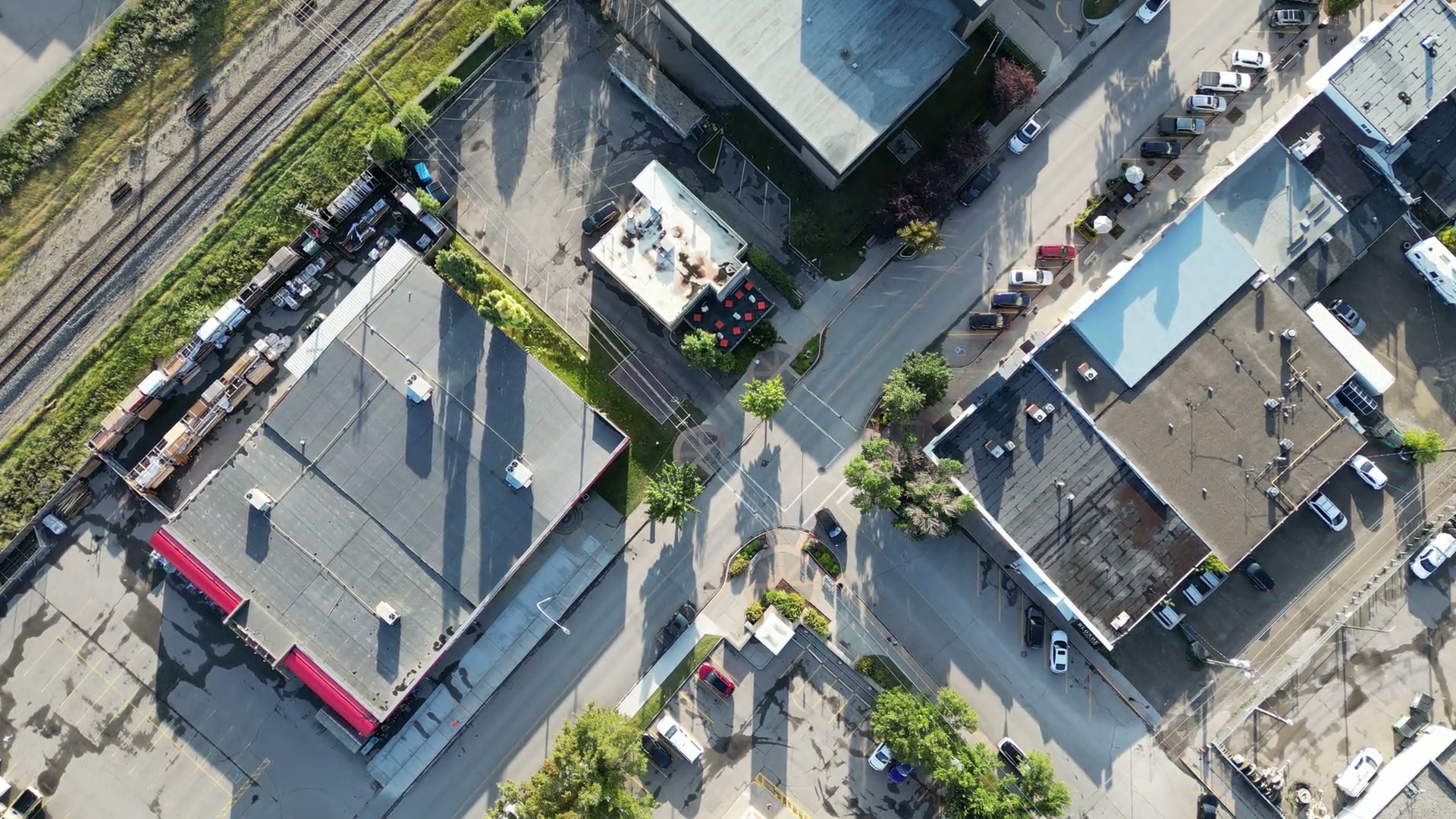 Straight down over 1st Street West in Cochrane: the rooftops of the block, parked cars along the kerb and the rail line running past