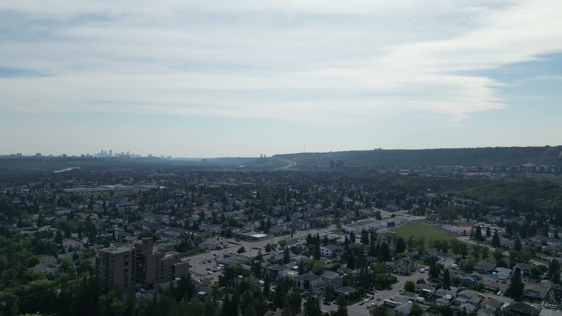 Panning right at half speed from the Bow across the roofs of Bowness in Calgary, past a brick apartment block, to downtown's towers on the horizon and a ski-jump in-run on the southern hill