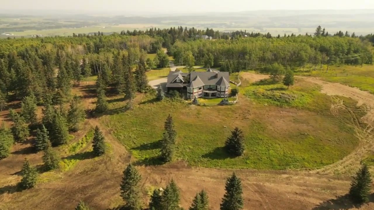 Aerial arc around a large country house on a treed ridge above the foothills