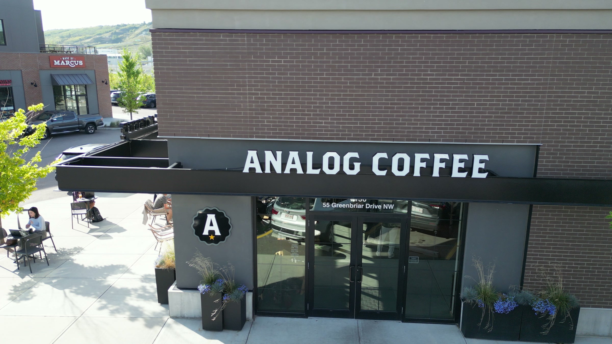 The café's front: brick, a black awning, a patio in morning sun