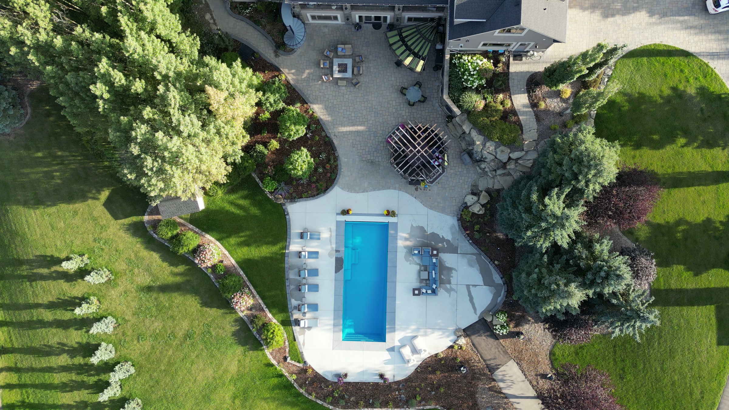 The pool from directly above: water, deck, loungers and the shadows of spruce